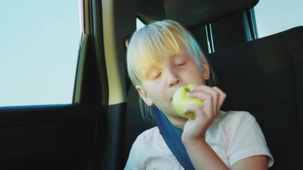 Une fillette de 6 ans mange une pomme dans une voiture. Faim facile et collation sur la route — Video