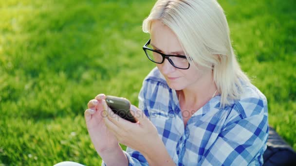Portrét mladé ženy nosit brýle, těší smartphone v parku. Pohled shora — Stock video