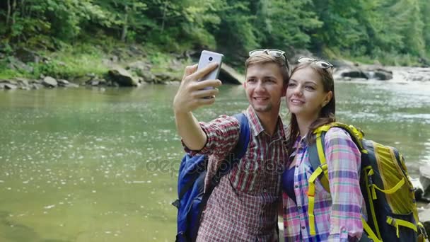 Мужчина с подругой фотографируются на фоне горной реки. В пасмурный день — стоковое видео