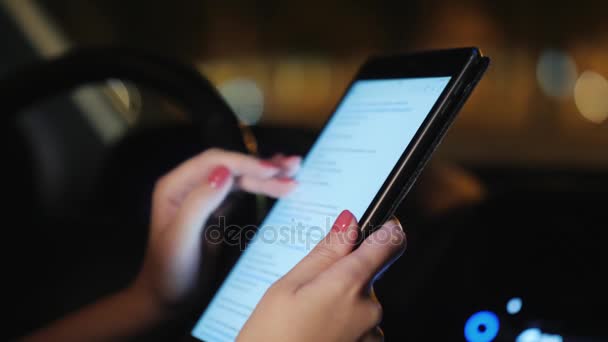 Une femme utilise une tablette à l'intérieur de la voiture. Le soir, la circulation des voitures est visible à l'extérieur de la fenêtre. Dans le cadre ne sont visibles que les mains — Video