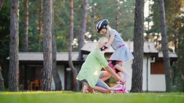 幸せな子供時代。若い母親は、娘にローラー スケートを配置するのに役立ちます。自分の家の裏庭に — ストック動画