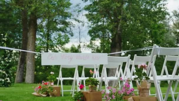 Grüner Rasen mit Reihen weißer Holzstühle. Im Vordergrund die Platte, von der unsere Geschichte hier ausgeht — Stockvideo