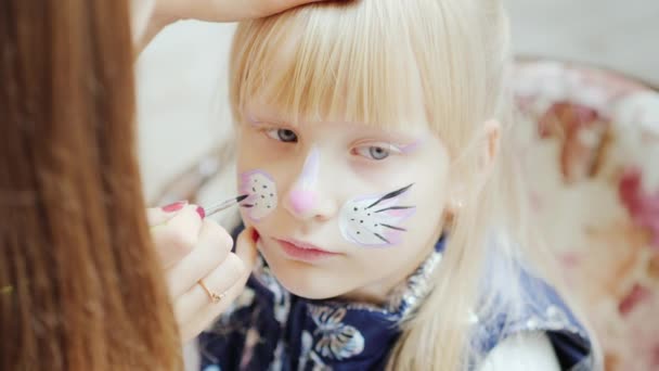 The child is applied with aquagrim. Tassel draws a cat mask. Concept - childrens holiday — Stock Video