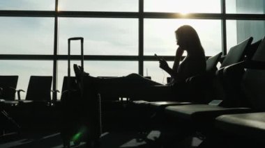 Havaalanı terminal içinde başarılı bir kadın silueti. Uçuş için bekleyen bir akıllı telefon ve kulaklık kullanır