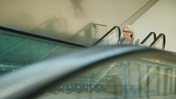 Business woman with travel bag and tablet rides on the escalator in the airport terminal or subway — Stock Video