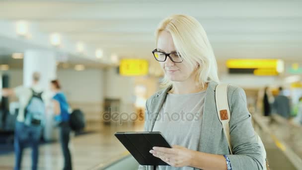 Деловая женщина в терминале международного аэропорта. Едет на движущейся ленте эскалатора, использует планшет — стоковое видео