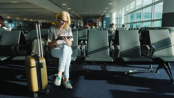 Молода жінка чекає на свій політ. Сидить у терміналі аеропорту, використовує планшет — стокове відео