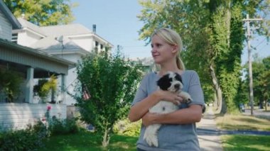 Genç bir kadın ile köpek yavrusu kucağında tipik bir Amerikan kasabasında cadde boyunca yürüyor. Yürüyüşe favori evcil hayvan