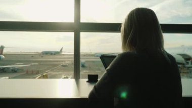 Bir kadın Havaalanı terminal penceresi masada oturur, bir tablet sahiptir. Her zaman online, konfor seyahat