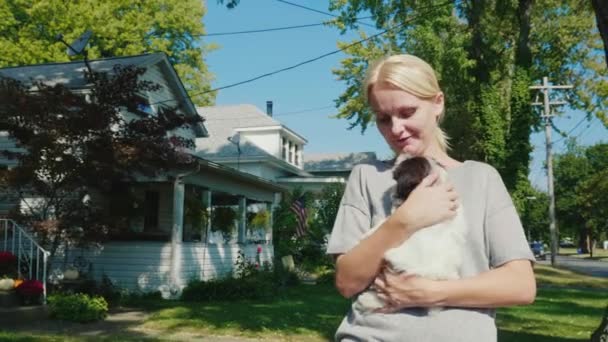 Op een wandeling met uw favoriete huisdier. Een vrouw loopt met een puppy in haar armen. Wandelen langs de typische straat van een kleine Amerikaanse stad — Stockvideo