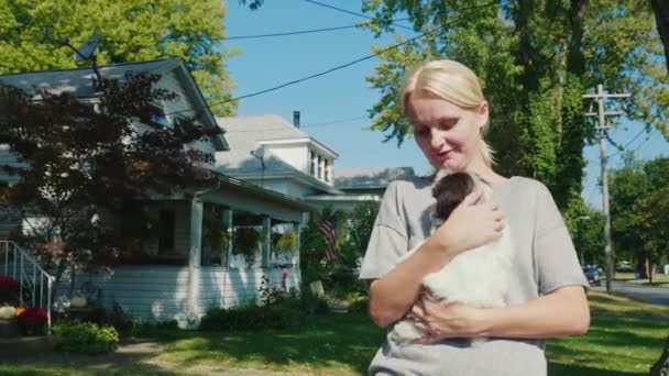 En promenade avec votre animal préféré. Une femme marche avec un chiot dans les bras. Marcher le long de la rue typique d'une petite ville américaine — Video