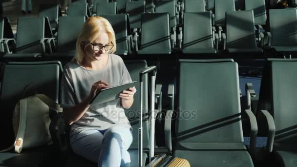 Кавказская женщина ждет своего рейса. Сидят в терминале аэропорта, пользуются планшетом — стоковое видео