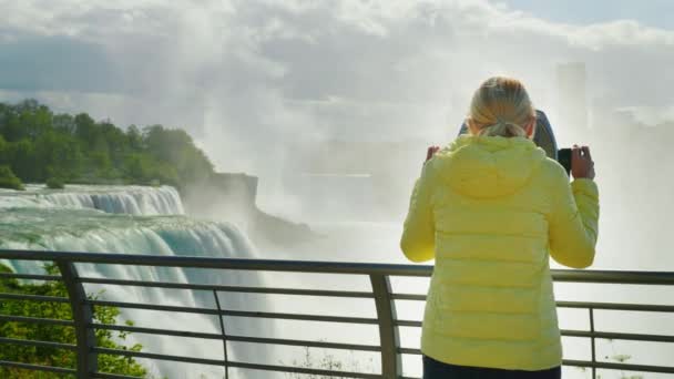 Una mujer mira las Cataratas del Niágara a través de unos prismáticos operados con monedas. El turismo en los Estados Unidos — Vídeo de stock
