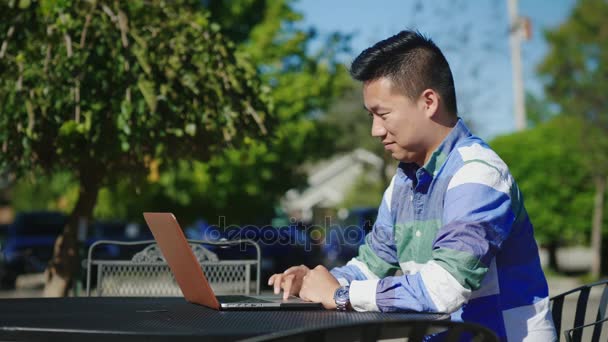 年轻的中国男子使用笔记本电脑。在咖啡馆的夏日露台 — 图库视频影像