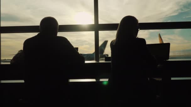 Силуэты людей, работающих с устройствами возле окна терминала аэропорта — стоковое видео