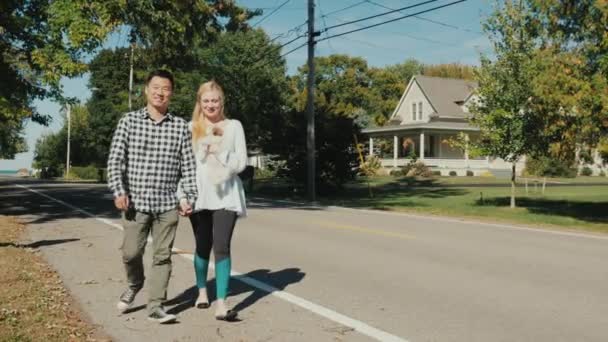 Ein Paar läuft die Straße entlang, eine Frau trägt einen Welpen auf den Händen. typische Straße einer Kleinstadt in den USA — Stockvideo