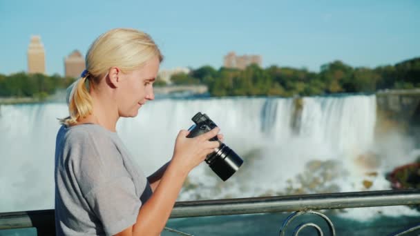 A woman looks through the photos on the camera screen. Against the background of a beautiful waterfall. Excellent memory of the holiday — Stock Video