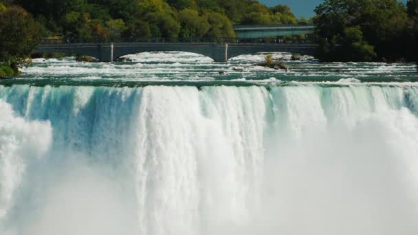 De watermuur van de Niagara watervallen en de brug over de rivier. Trage beweging 180 fps video — Stockvideo