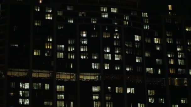 Edificio de oficinas en la oscuridad. Las ventanas están iluminadas, las siluetas de la gente son visibles. Tilt shot — Vídeo de stock