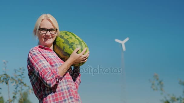 Портрет женщины-фермера. Он смотрит в камеру, держа в руках арбуз. Хорошая концепция урожая — стоковое видео