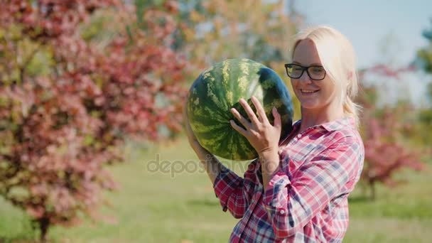 Outono e uma colheita generosa. Uma mulher agricultora está segurando uma grande melancia pesada — Vídeo de Stock