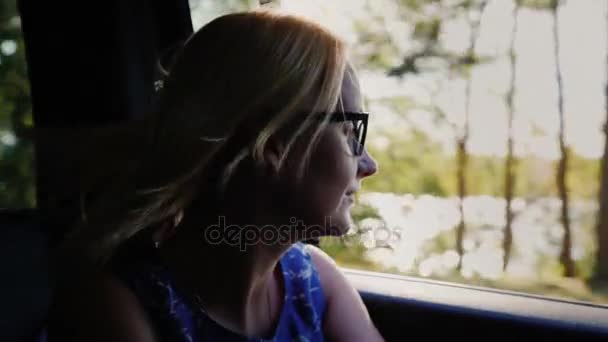 Женщина смотрит в окно машины. Ветер играет с ее волосами, красивыми подсветками и тенями. Путешествие в машине — стоковое видео