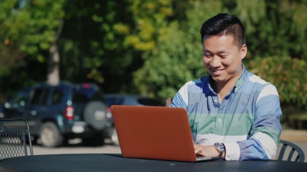 Nöjd asiatiska man arbetar med laptop på sommarterrassen — Stockvideo
