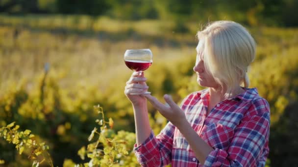 Una mujer está probando vino. Está cerca del viñedo al atardecer. — Vídeos de Stock