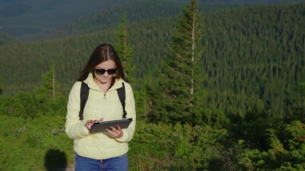 स्टेटिक शॉट: जंगल से ढकी पहाड़ों की एक सुरम्य पृष्ठभूमि पर एक स्मार्टफोन का आनंद लेने वाली युवा महिला। हमेशा ऑनलाइन — स्टॉक वीडियो