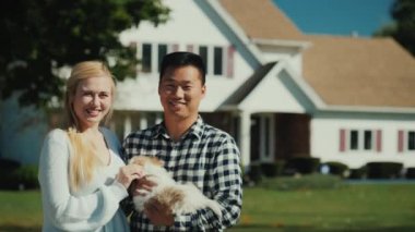 Elinde bir köpek yavrusu ile genç bir çok etnik gruptan oluşan çift portresi. Kameraya bak, evlerinin önünde stand