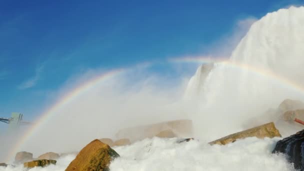 Am Fuße der Niagarafälle. Wasserläufe werden gegen Felsen gebrochen, ein Regenbogen über einem Wasserfall ist zu sehen — Stockvideo
