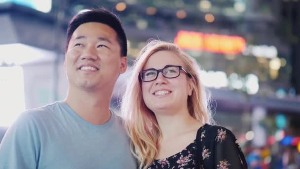 Una joven pareja multiétnica en una ciudad nocturna. Con admiración miran a su alrededor. Times Square, Nueva York — Vídeos de Stock