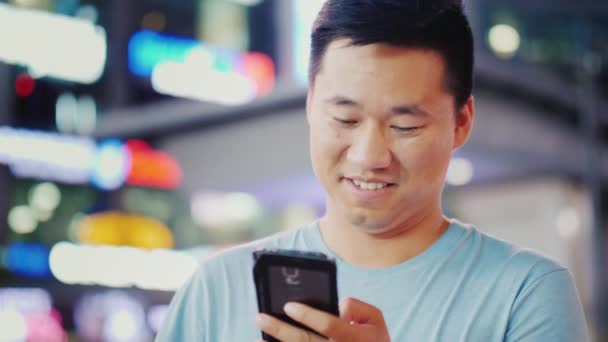 Ein attraktiver junger Mann nutzt nachts ein Smartphone in einer Großstadt. um die Lichter der Werbung und Wolkenkratzer. quadratisch, new york — Stockvideo