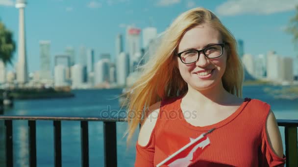 Donna con una bandiera canadese sullo sfondo di Toronto. Sorridendo, guardando la macchina fotografica — Video Stock