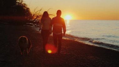 Siluetleri romantik bir çift. Göl ya da deniz yakınındaki bir köpekle günbatımında yürüyüş