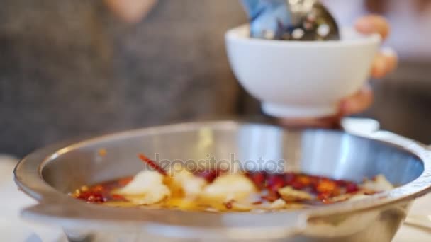 Женщина наливает ему в тарелку острый суп из морепродуктов. Куски рыбы плавают в бульоне со специями. Аутентичная китайская кухня — стоковое видео