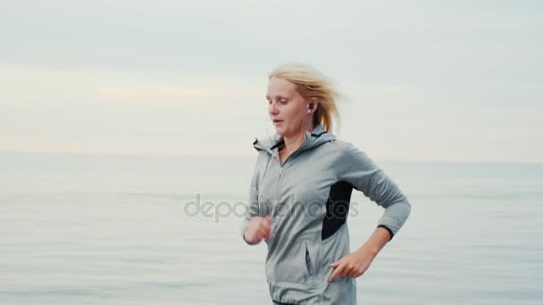 Активная женщина средних лет. Женщина бегает на фоне спокойного моря или озера — стоковое видео