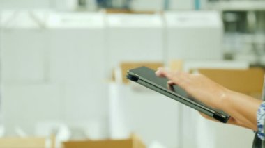 Lojistik ve stok muhasebe. Bir tablet ile bir yığın beyaz kutularının arka plan üzerinde çalışan kadın