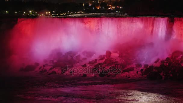 Evening illumination of the famous Niagara Falls. Water jets are lit by red light from the Canadian coast — Stock Video