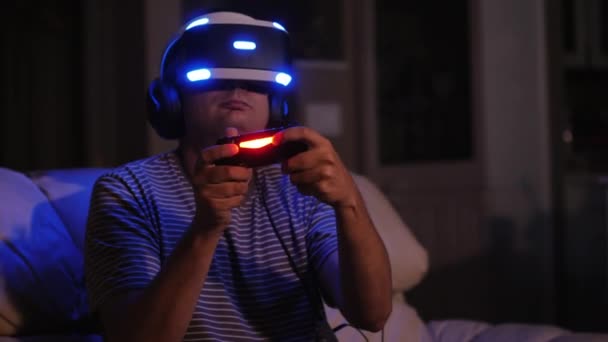 Um jogador homem com paixão joga no capacete da realidade virtual. Tarde da noite, conceito de vício em jogo — Vídeo de Stock