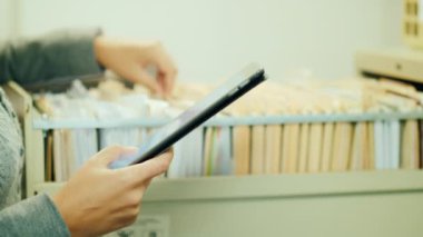 Kadın içinde arşiv işleri, çekmecede girdilerle görünüyor. Bir tablet kullanır