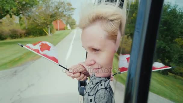 A woman is looking out of the car window, holding a Canadian flag in her hand — Stock Video