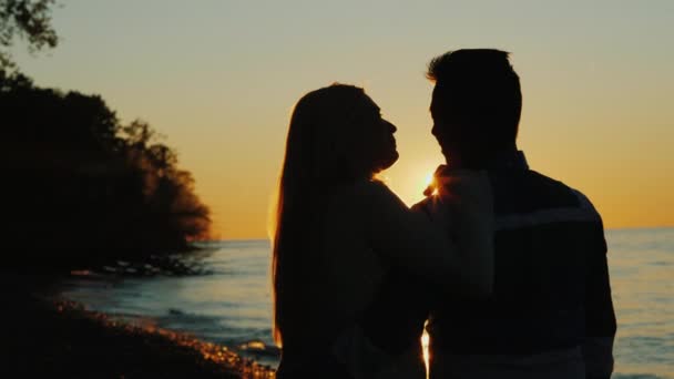 Mężczyzna i kobieta o zachodzie słońca w pobliżu morza. Promienie słońca świecą pięknie od tyłu — Wideo stockowe