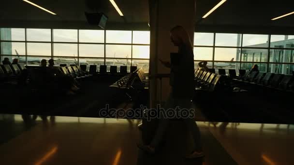 Una mujer de negocios con un smartphone en la mano y un montón de equipaje pasea por la terminal del aeropuerto internacional. — Vídeos de Stock
