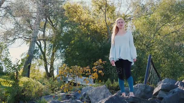 Жінка стоїть на скелях на озері, дивлячись на відстань — стокове відео