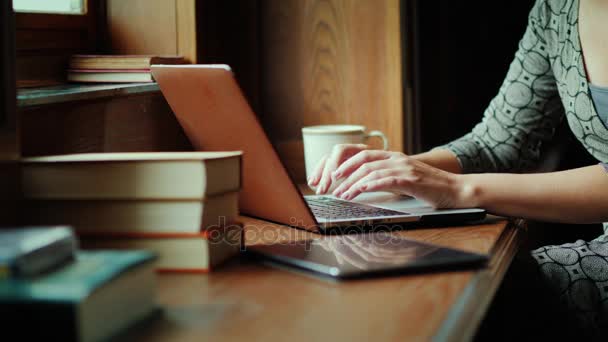 Une femme travaille avec un ordinateur portable à la bibliothèque. A proximité se trouvent des livres, gros plan - seules les mains sont visibles dans le cadre — Video
