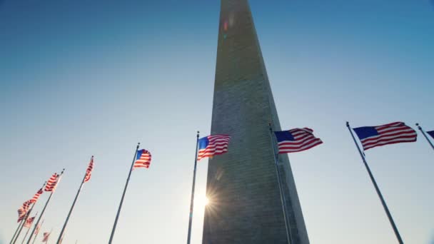 Dönthető lövés: A nap úgy tűnik, mert a Washington emlékmű. Amerikai zászlók, juharfalevél fedél alatt — Stock videók