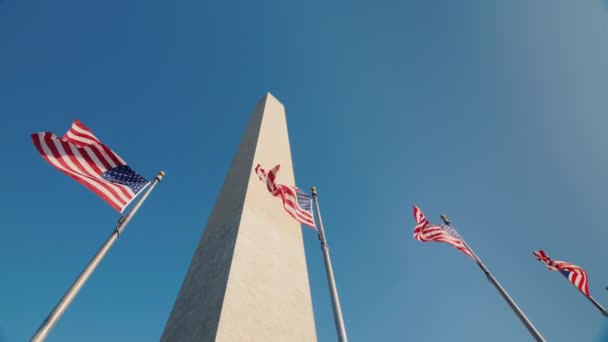 Низький кут пострілу монумент Вашингтона у Вашингтоні, США, американські прапори клапоть нижче — стокове відео