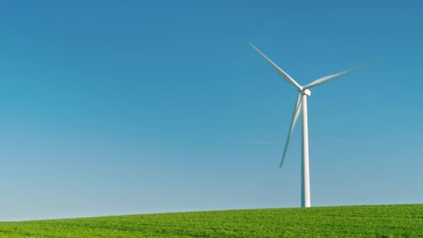 L'éolienne industrielle se trouve sur une colline verdoyante. Sur le fond du ciel bleu, une image idylistique de l'énergie pure — Video