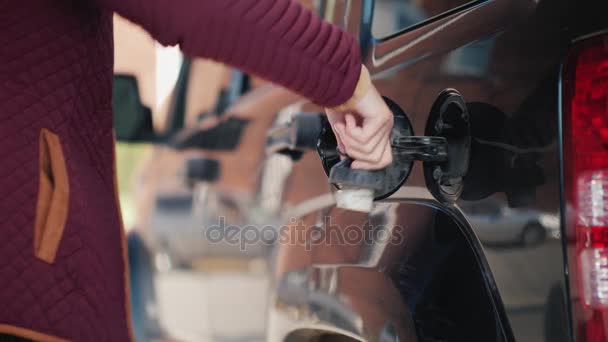 Женщина управляет своей чёрной машиной. Открывает люк и вставляет пистолет для заправки — стоковое видео